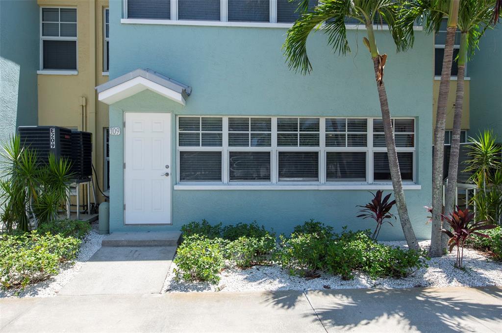 The exterior of a teal-colored residential unit features a white front door and large windows — 19417 GULF BOULEVARD UNIT E109, INDIAN ROCKS BEACH, FL
