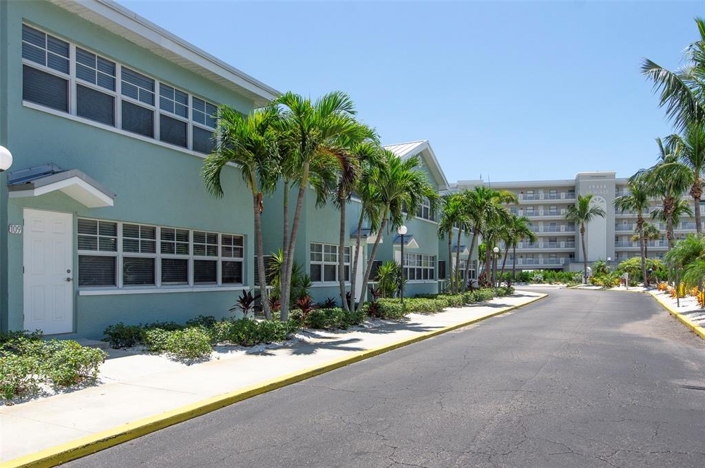 A two-story teal apartment building with palm trees and a paved road in front — 19417 GULF BOULEVARD UNIT E109, INDIAN ROCKS BEACH, FL
