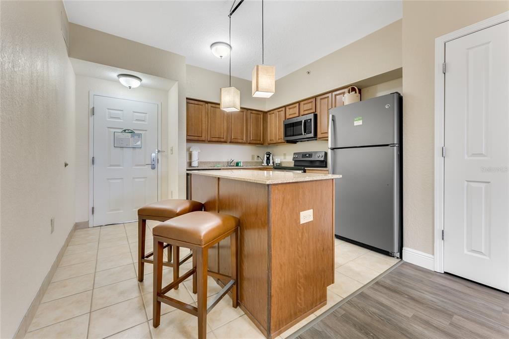 A kitchen features wood cabinets, granite countertops, a kitchen island with stools, and stainless appliances — 12556 FLORIDAYS RESORT DRIVE UNIT A-307, ORLANDO, FL