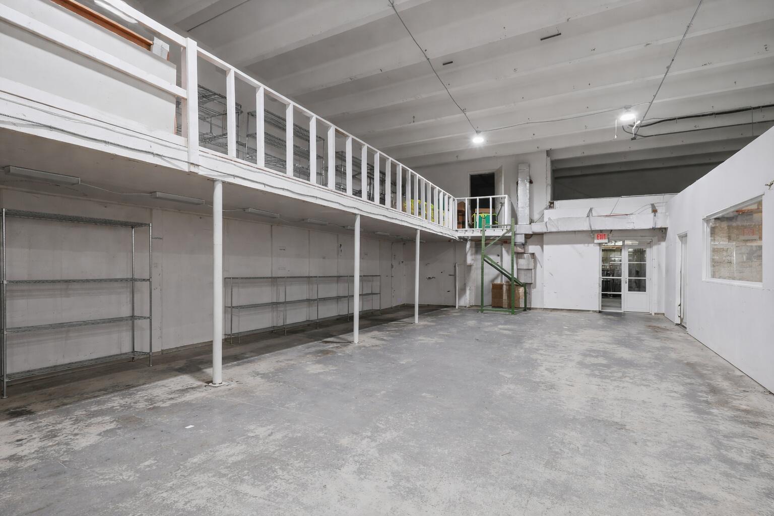An industrial warehouse space features a concrete floor, metal shelving, and an elevated mezzanine level — 1800 N Dixie Highway, Hollywood FL 33020, HOLLYWOOD, FL