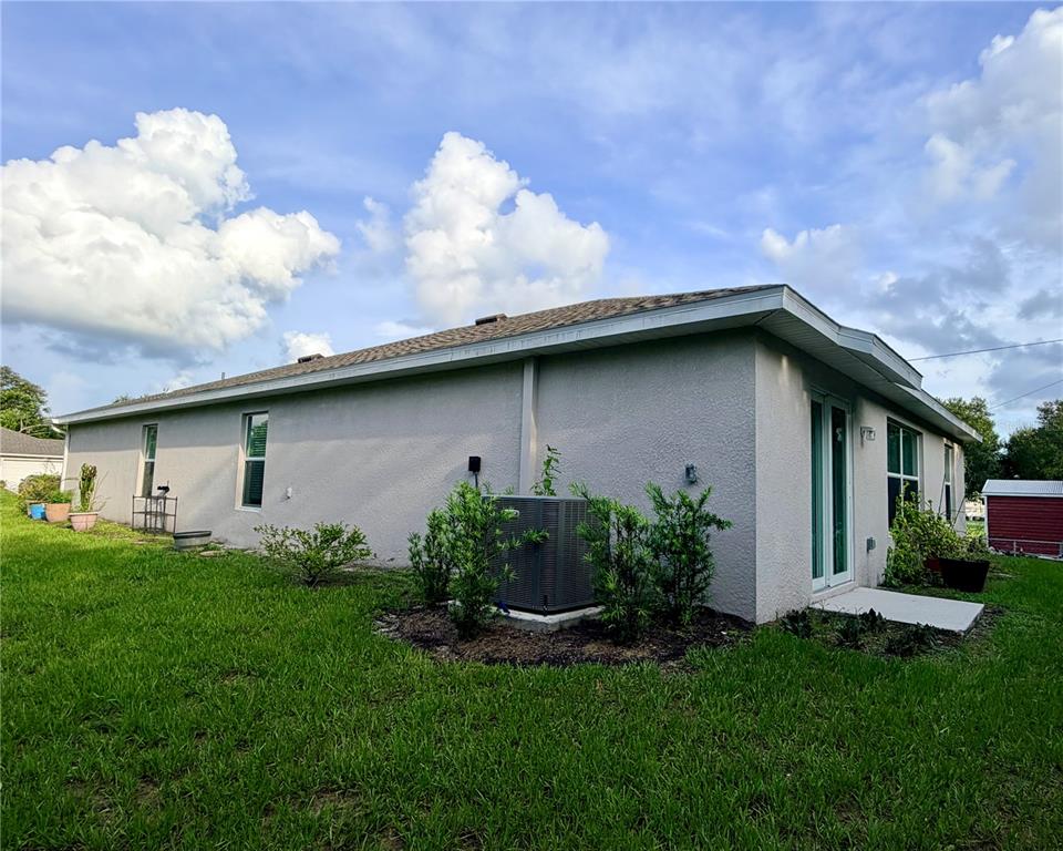 The exterior of a single-story house features light gray stucco walls and a central air conditioner — 1485 PULASKI STREET, PORT CHARLOTTE, FL