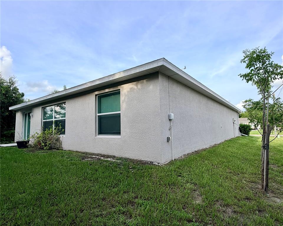 A view of the side and rear exterior of a light-colored stucco house — 1485 PULASKI STREET, PORT CHARLOTTE, FL