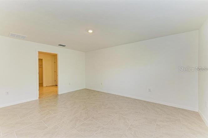 An empty room features light-colored tile flooring, white walls, and a doorway leading to another space — 1485 PULASKI STREET, PORT CHARLOTTE, FL