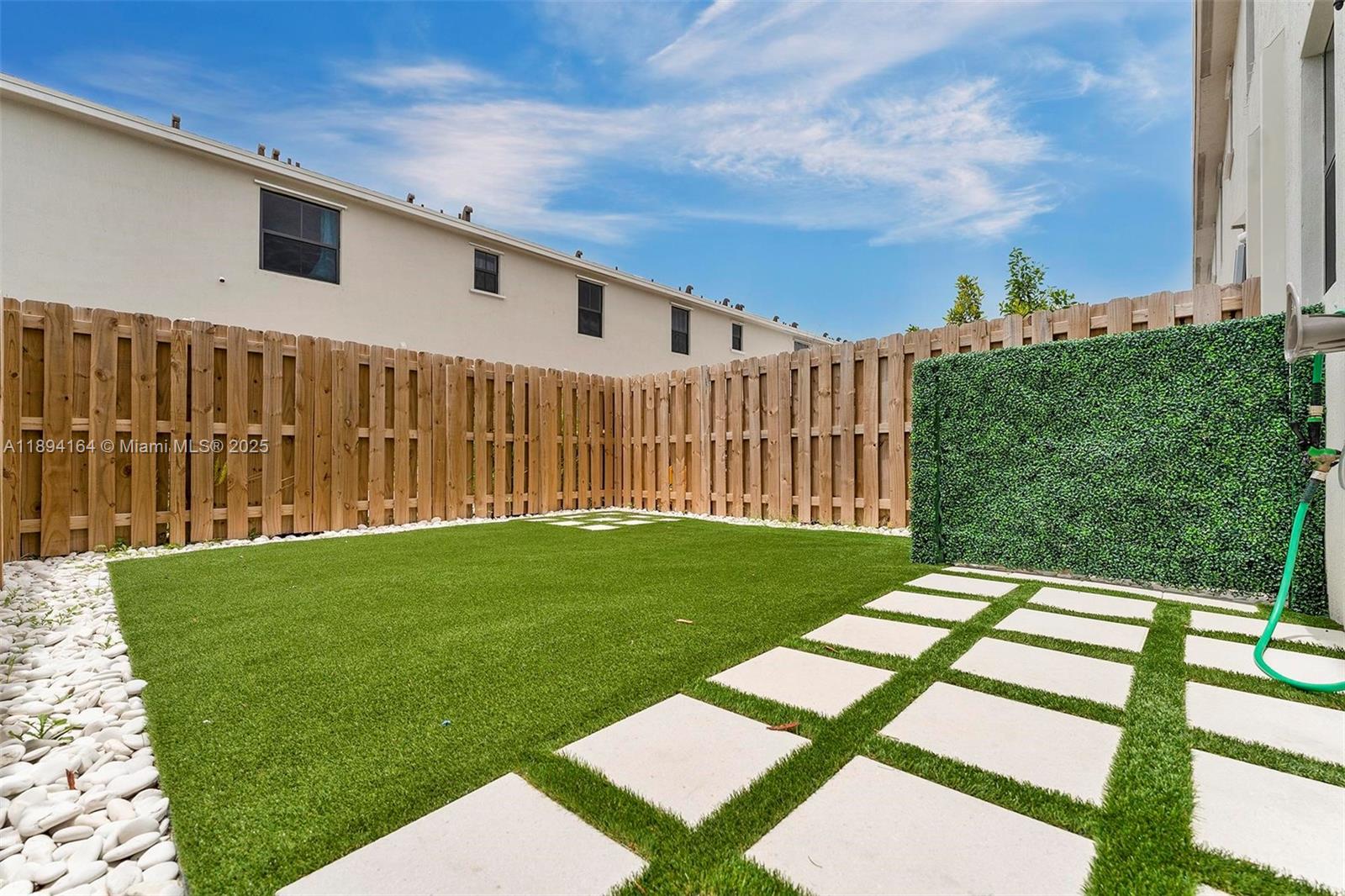 A backyard features artificial turf, white stone borders, square pavers, and a wooden privacy fence — 450 NE 13th St, Florida City FL 33034, FLORIDA CITY, FL