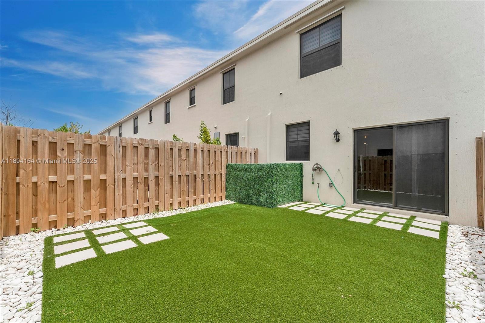 A fenced backyard features artificial turf, white stone borders, and a sliding glass door entrance — 450 NE 13th St, Florida City FL 33034, FLORIDA CITY, FL