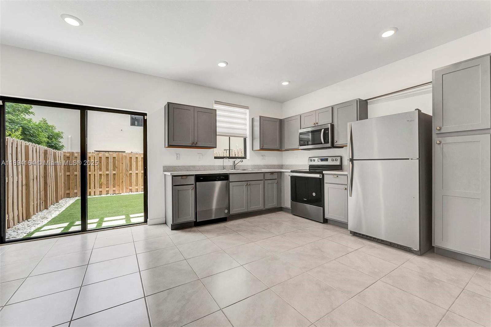 A kitchen features gray cabinets, stainless steel appliances, tile flooring, and a sliding glass door — 450 NE 13th St, Florida City FL 33034, FLORIDA CITY, FL