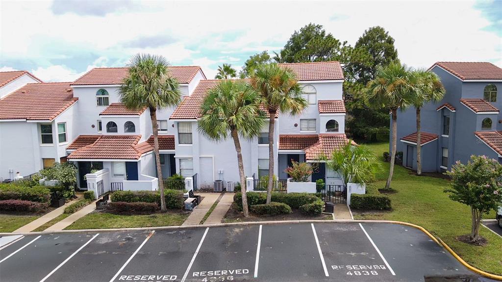 An exterior view of a multi-story townhouse complex with palm trees and reserved parking spaces — 4836 MARKS TERRACE UNIT 394, ORLANDO, FL