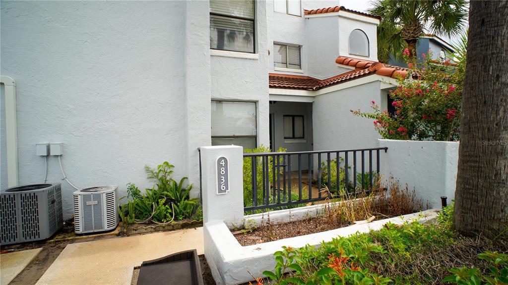 An exterior view of a white stucco townhouse with a small gated courtyard and AC units — 4836 MARKS TERRACE UNIT 394, ORLANDO, FL