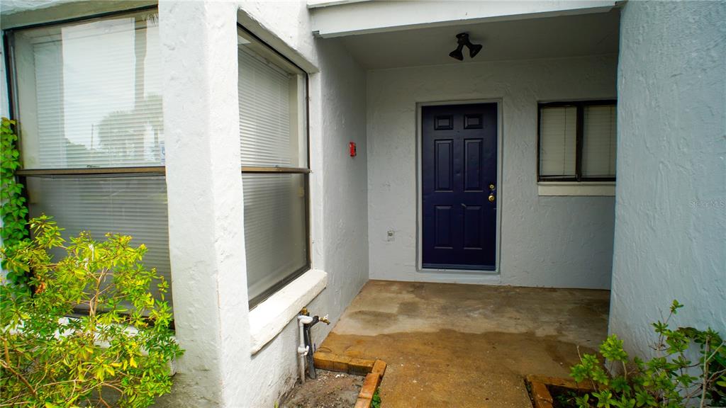 A covered entryway with a blue front door, two windows, and small garden beds — 4836 MARKS TERRACE UNIT 394, ORLANDO, FL