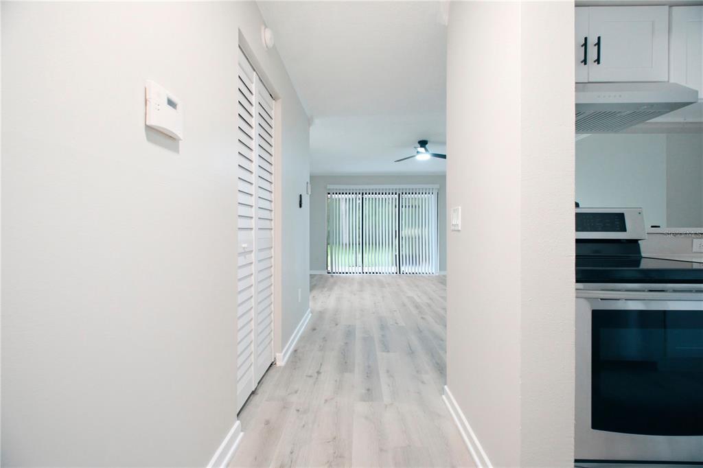 A hallway with light wood-look flooring leads to a living area with sliding glass doors — 4836 MARKS TERRACE UNIT 394, ORLANDO, FL
