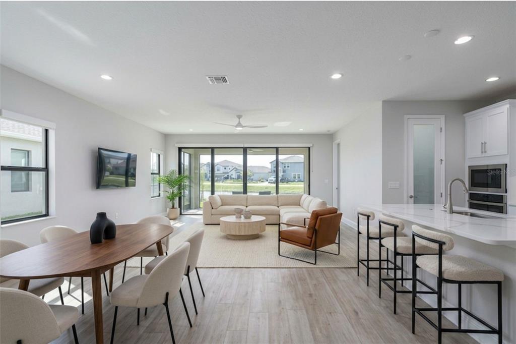 An open-concept living and dining area features light wood floors, a sectional sofa, and kitchen — 13419 HEARTWOOD WAY, PARRISH, FL