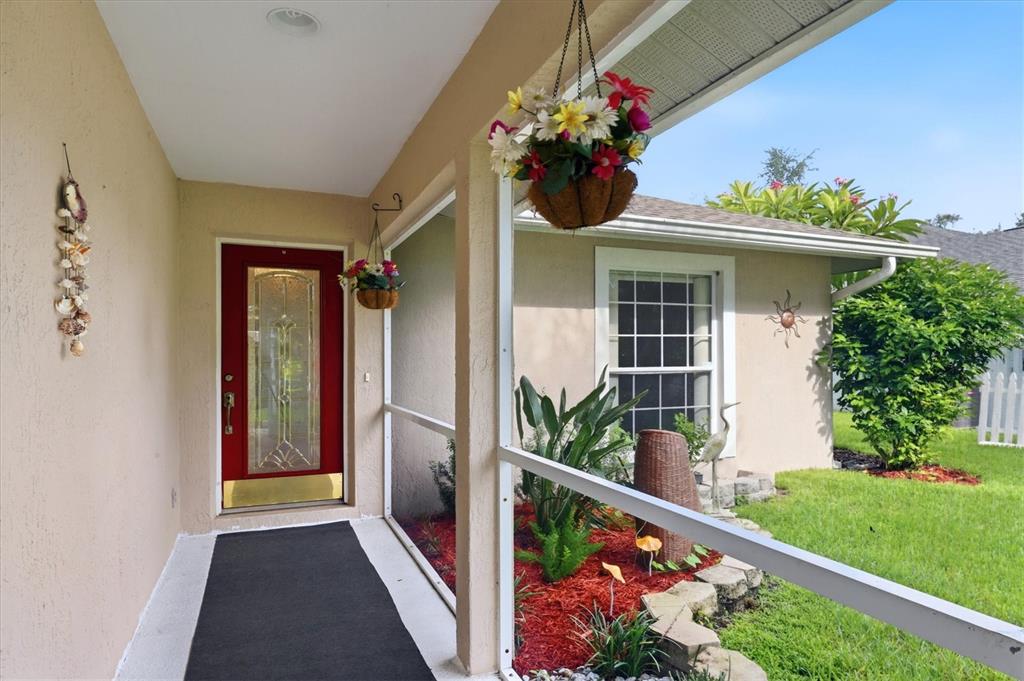 A covered front porch features a red door, a black mat, and hanging flower baskets — 4380 IOLA DRIVE, SARASOTA, FL