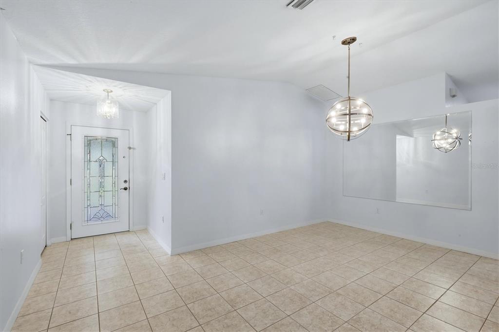 An entryway and dining area with tile flooring, a glass-paneled front door, and globe chandeliers — 4380 IOLA DRIVE, SARASOTA, FL