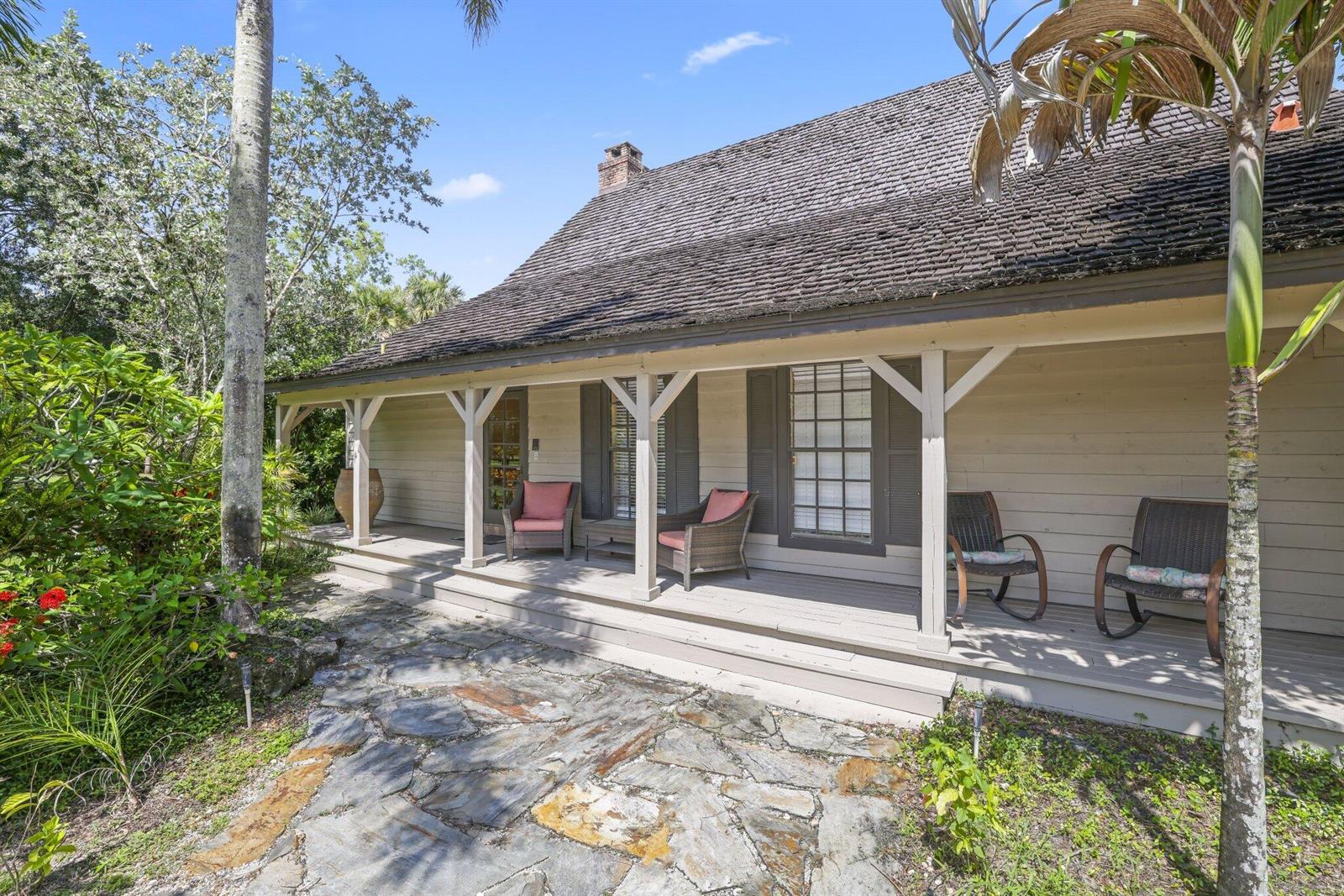 A wooden house with a covered porch, stone walkway, and rocking chairs sits outdoors — 790 E Rambling Drive, Wellington FL 33414, WELLINGTON, FL