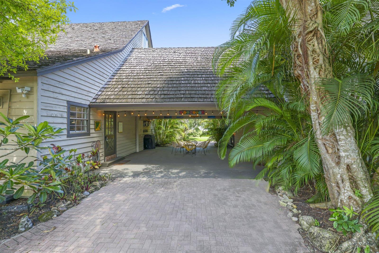 A paved driveway leads to a covered carport area with string lights and outdoor seating — 790 E Rambling Drive, Wellington FL 33414, WELLINGTON, FL