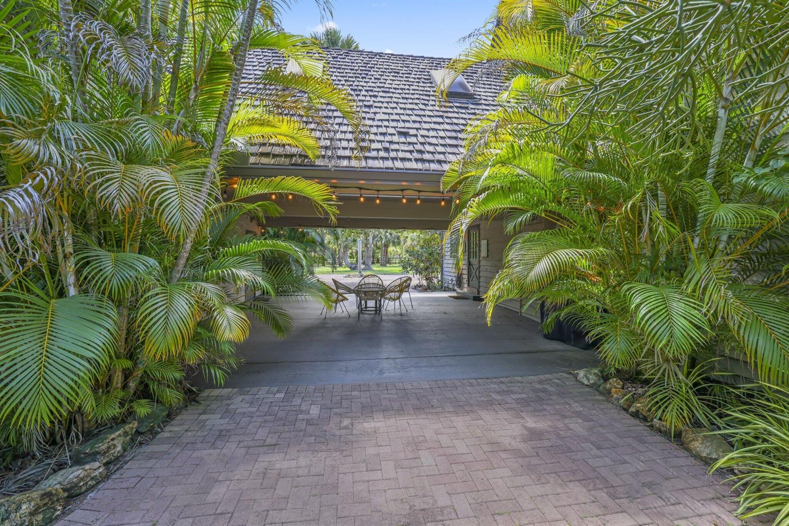 A paved driveway leads to a covered patio area framed by lush palm trees — 790 E Rambling Drive, Wellington FL 33414, WELLINGTON, FL