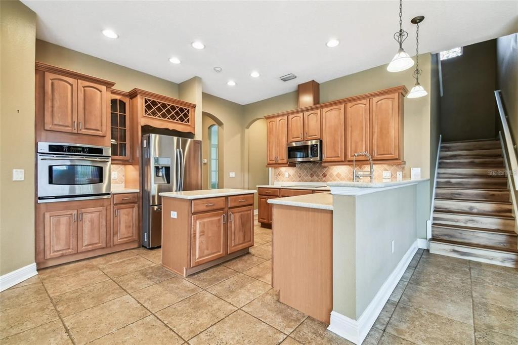 A kitchen with wood cabinets, stainless steel appliances, a center island, and stairs nearby — 1110 FACET VIEW WAY, VALRICO, FL