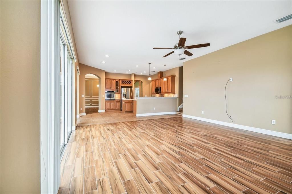 An open-concept living room with wood-look tile flooring leads into a kitchen with wooden cabinets — 1110 FACET VIEW WAY, VALRICO, FL