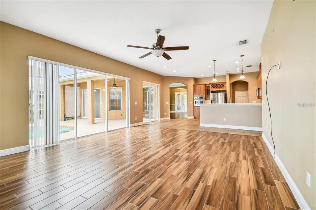 A spacious living area features wood-look tile floors, a ceiling fan, and sliding glass doors — 1110 FACET VIEW WAY, VALRICO, FL