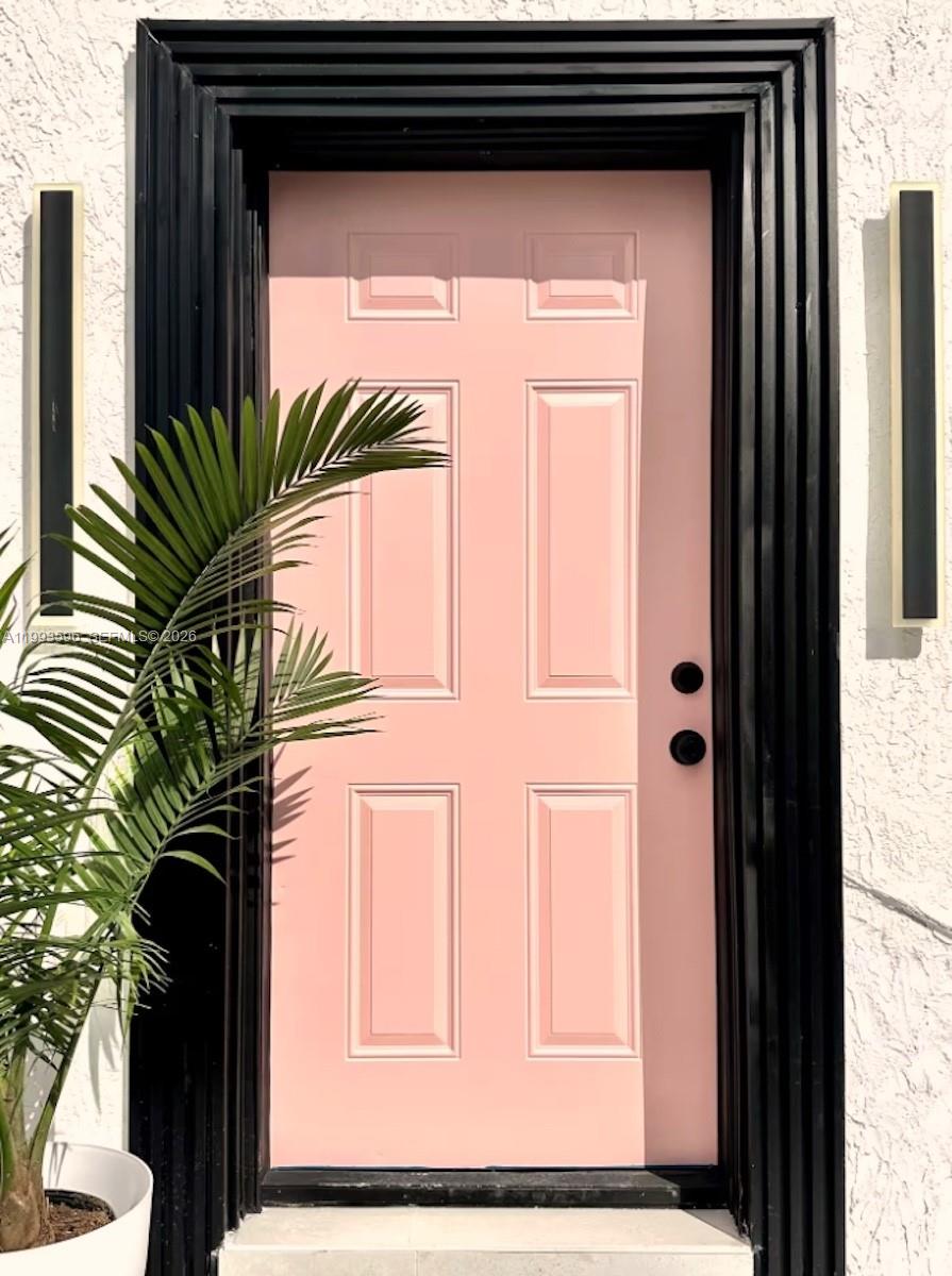 A pink front door with black trim and hardware is flanked by two vertical lights — 745 NW 47th Ter, Miami FL 33127, MIAMI, FL