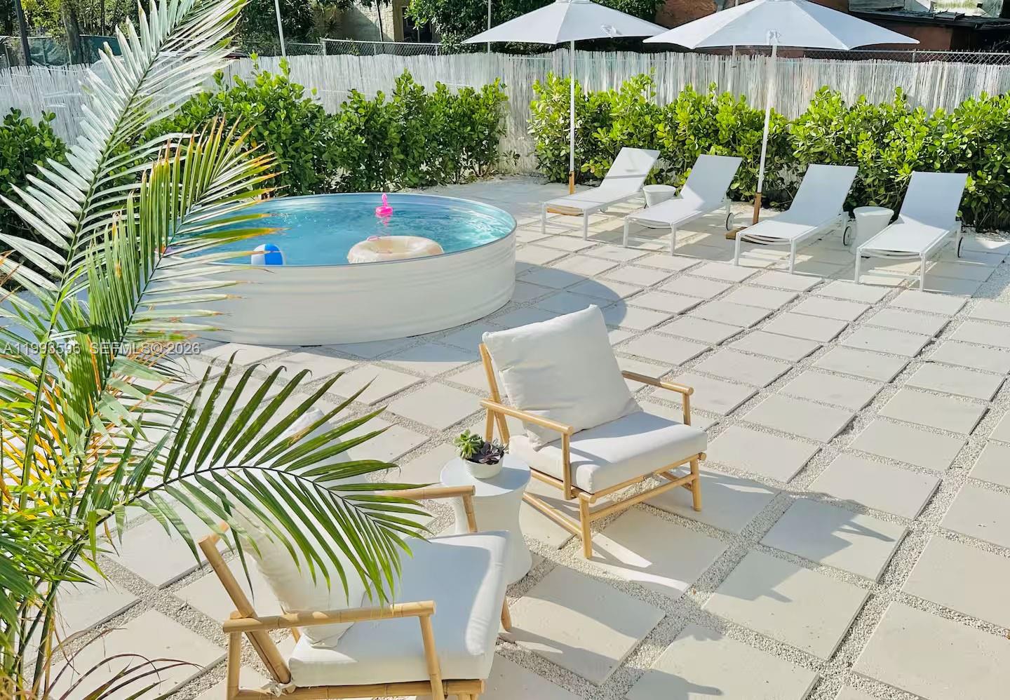 A backyard patio features a circular stock tank pool, lounge chairs, and white pavers — 745 NW 47th Ter, Miami FL 33127, MIAMI, FL