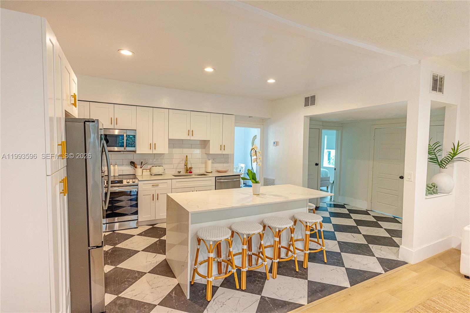 A kitchen features white cabinets, a marble-topped island with four stools, and checkered flooring — 745 NW 47th Ter, Miami FL 33127, MIAMI, FL