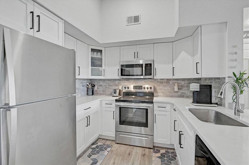 A kitchen features white cabinets, stainless steel appliances, quartz countertops, and a gray tiled backsplash — 4138 CENTRAL SARASOTA PARKWAY UNIT 1534, SARASOTA, FL