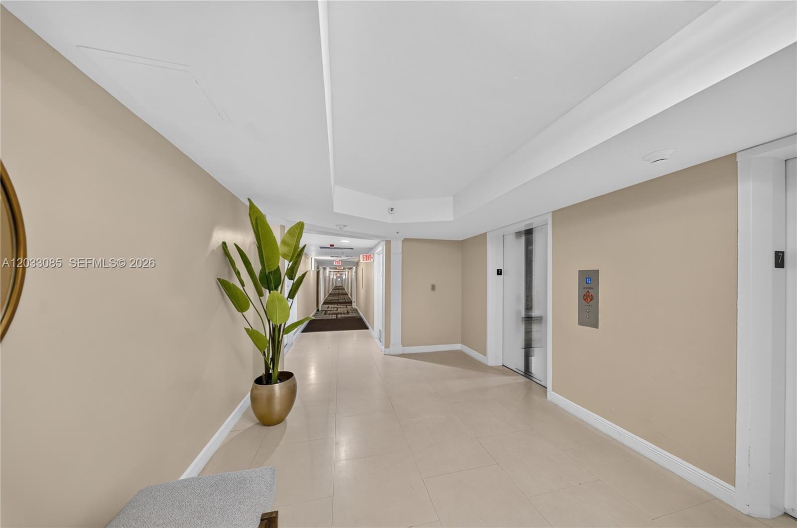 A hallway features beige walls, tile flooring, a potted plant, and an elevator entrance — 5600 Collins Ave # 7W, Miami Beach FL 33140, MIAMI BEACH, FL