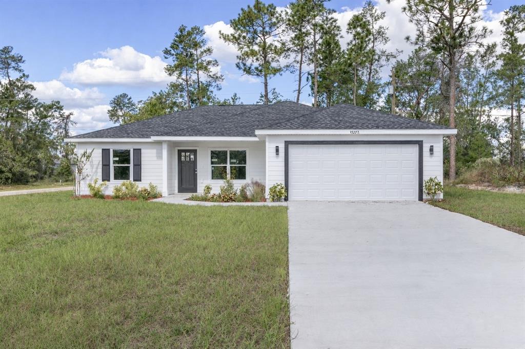 A single-story white house with a garage sits on a grassy lot with trees — 15429 SW 26TH PLACE, OCALA, FL