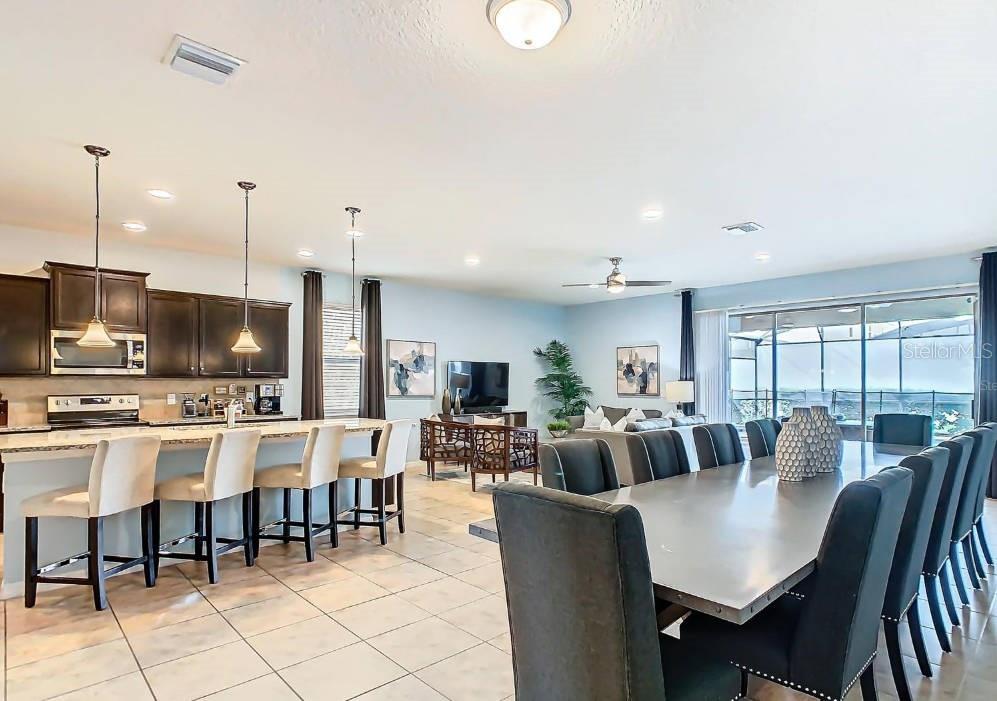 An open-concept kitchen and dining area with dark cabinetry, tile flooring, and a large table — 1602 LIMA AVENUE, KISSIMMEE, FL