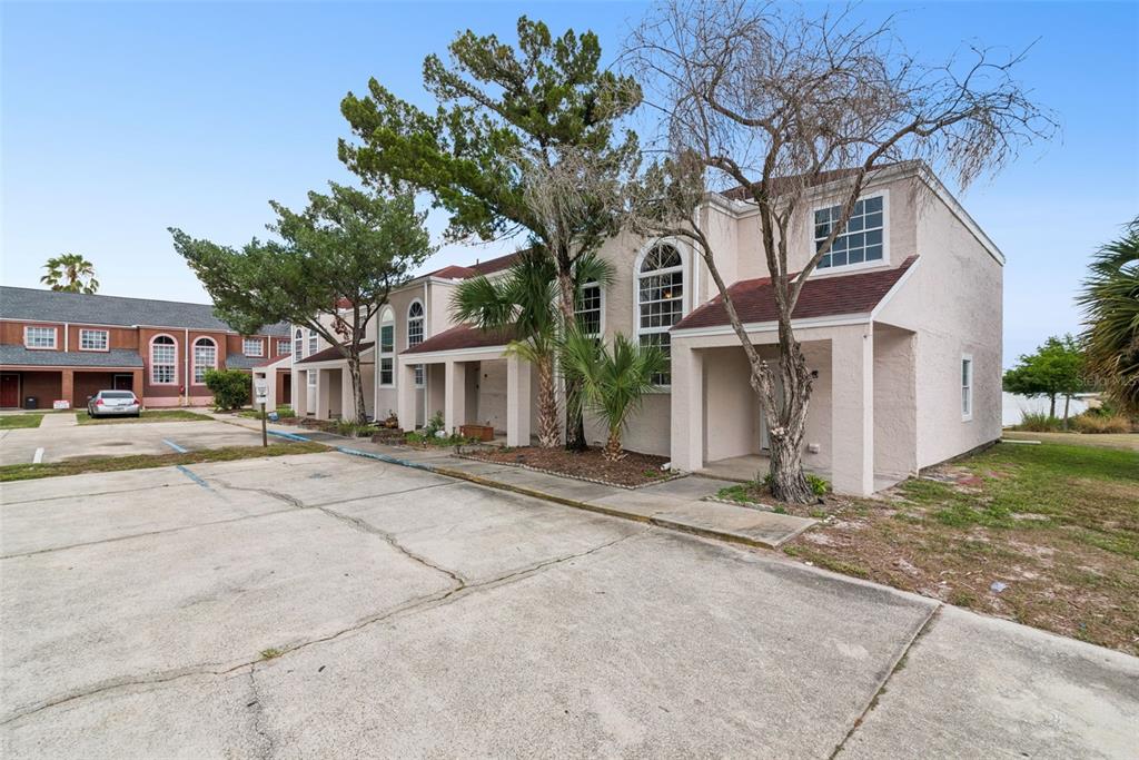 A row of two-story stucco townhomes with arched windows and a shared concrete parking lot — 214 MAJORS LANE UNIT F, KISSIMMEE, FL