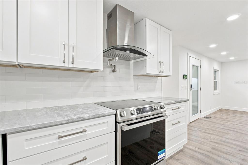 A modern kitchen features white cabinets, marble-look countertops, stainless steel appliances, and light wood flooring — 163 DOLPHIN DRIVE E, OLDSMAR, FL