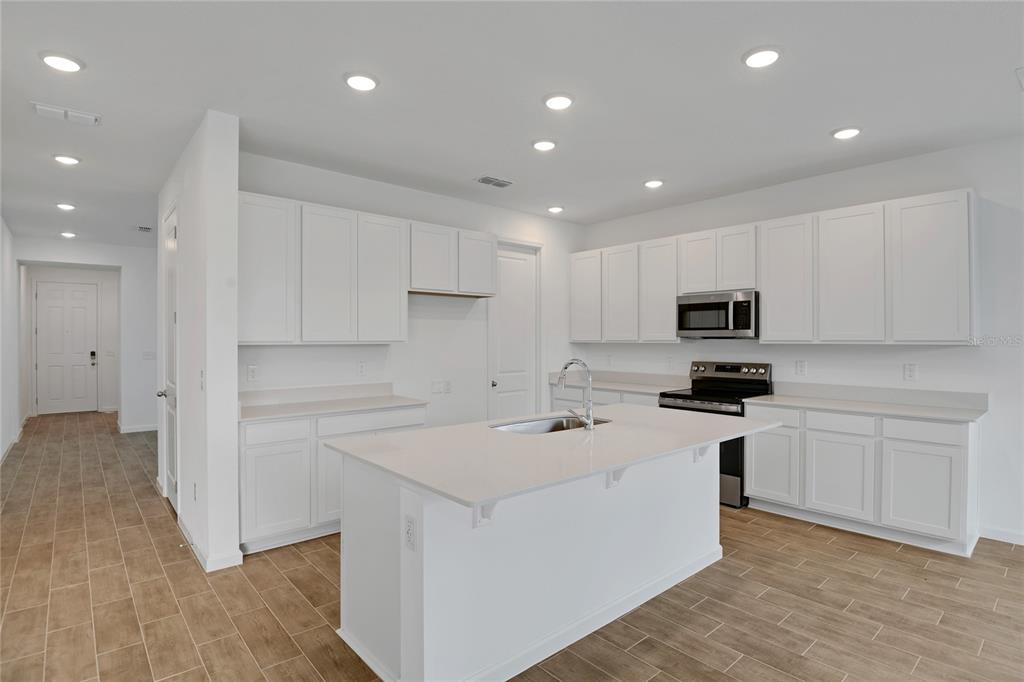 A white kitchen features a center island, quartz countertops, and light wood-look tile flooring — 330 ALEXANDRITE STREET, DELAND, FL