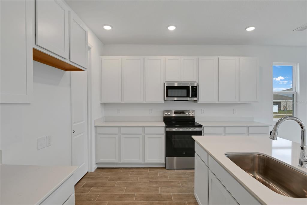 A modern kitchen features white cabinets, stainless steel appliances, and a central island with sink — 330 ALEXANDRITE STREET, DELAND, FL