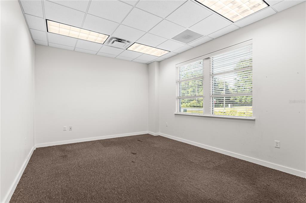 An empty office room features beige carpet, white walls, a drop ceiling, and large windows — 6515 NW 16TH STREET, GAINESVILLE, FL