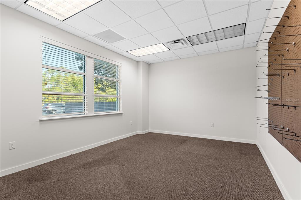 An empty office with brown carpet, white walls, a window with blinds, and a pegboard wall — 6515 NW 16TH STREET, GAINESVILLE, FL