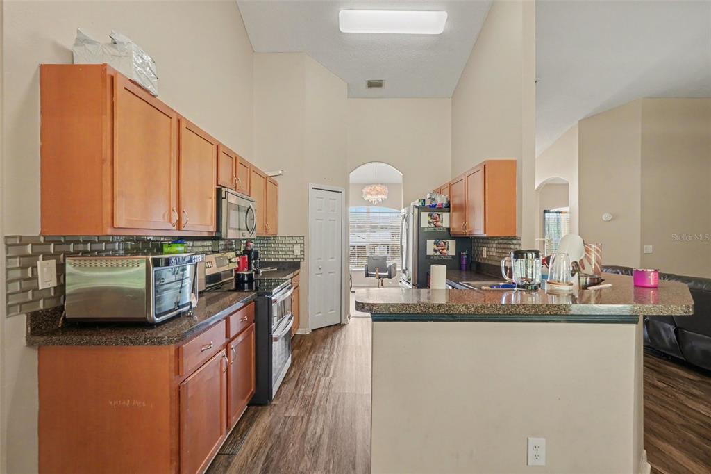 A kitchen with wood cabinets, granite countertops, a tile backsplash, and stainless steel appliances — 11222 MONTCALM ROAD, SPRING HILL, FL