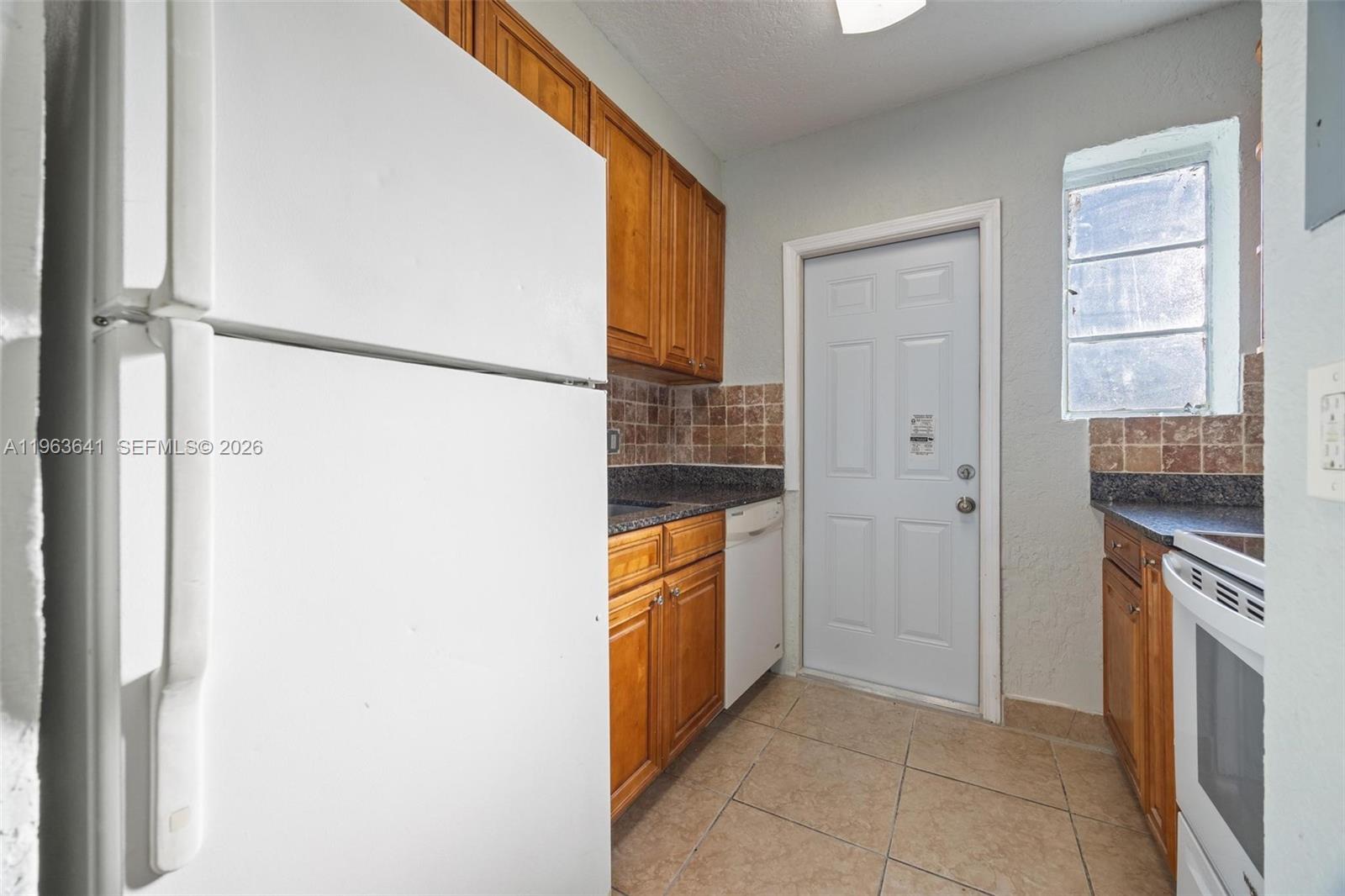 A kitchen features wood cabinets, dark countertops, tile flooring, and a white refrigerator — 2525 N 23rd Ave, Hollywood FL 33020, HOLLYWOOD, FL