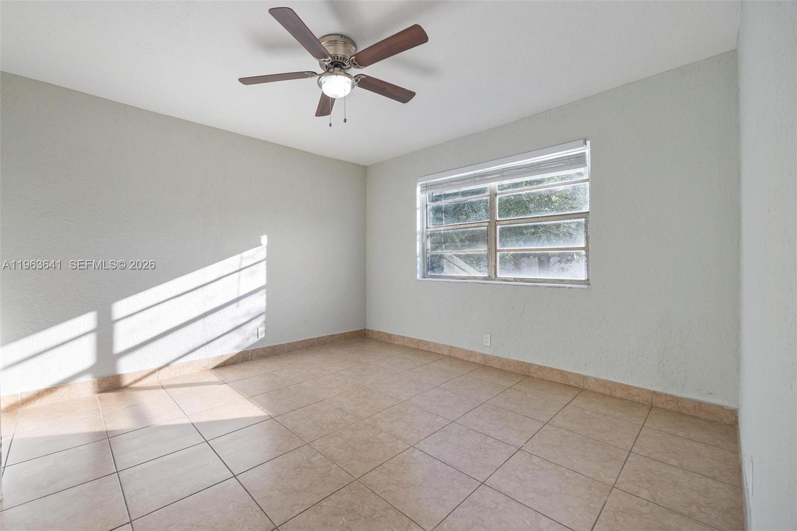 An empty room features light-colored walls, tile flooring, a ceiling fan, and a window — 2525 N 23rd Ave, Hollywood FL 33020, HOLLYWOOD, FL
