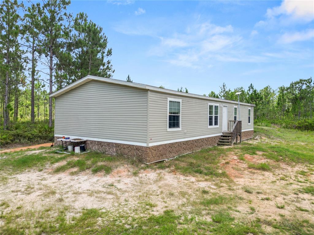 A single-story manufactured home with light siding and a stone-patterned foundation sits on a dirt lot — 3450 SALYERS ROAD, CLERMONT, FL