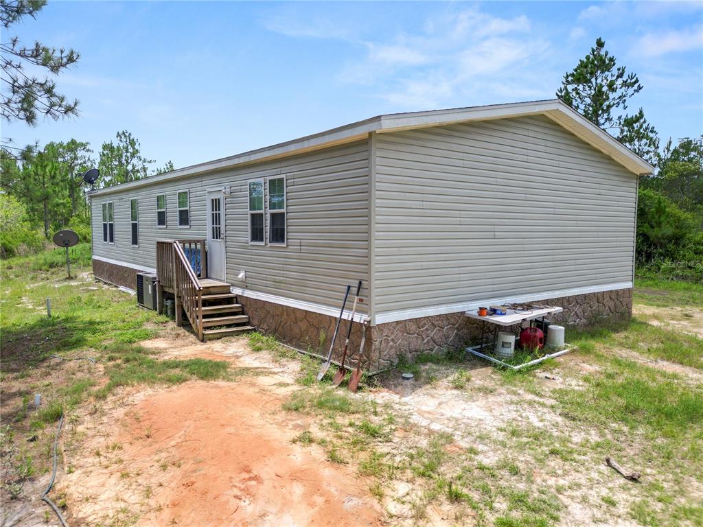 The exterior of a tan manufactured home with a wooden staircase and stone-patterned skirting — 3450 SALYERS ROAD, CLERMONT, FL