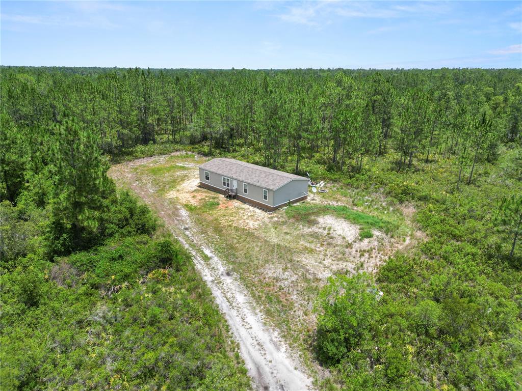 An aerial view shows a manufactured home situated on a cleared lot surrounded by forest — 3450 SALYERS ROAD, CLERMONT, FL