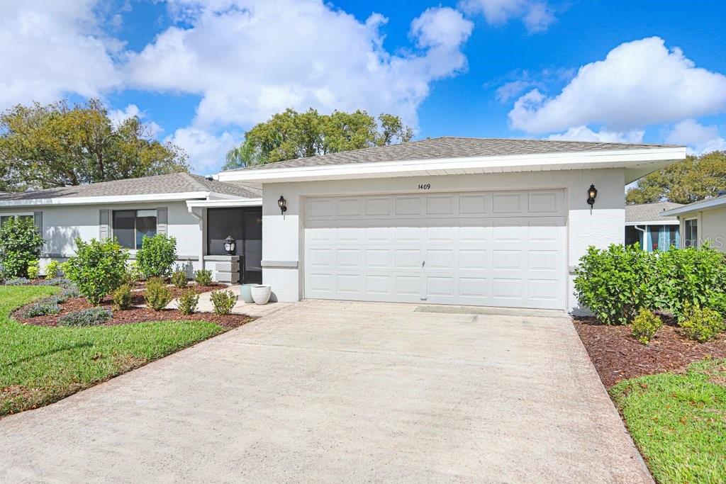 A single-story house with a white garage, gray roof, and landscaped front yard — 1409 INGRAM DRIVE UNIT 75, SUN CITY CENTER, FL