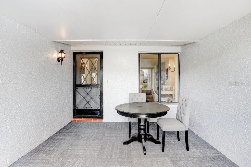 A covered patio features a round black table, two upholstered chairs, and a screen door — 1409 INGRAM DRIVE UNIT 75, SUN CITY CENTER, FL