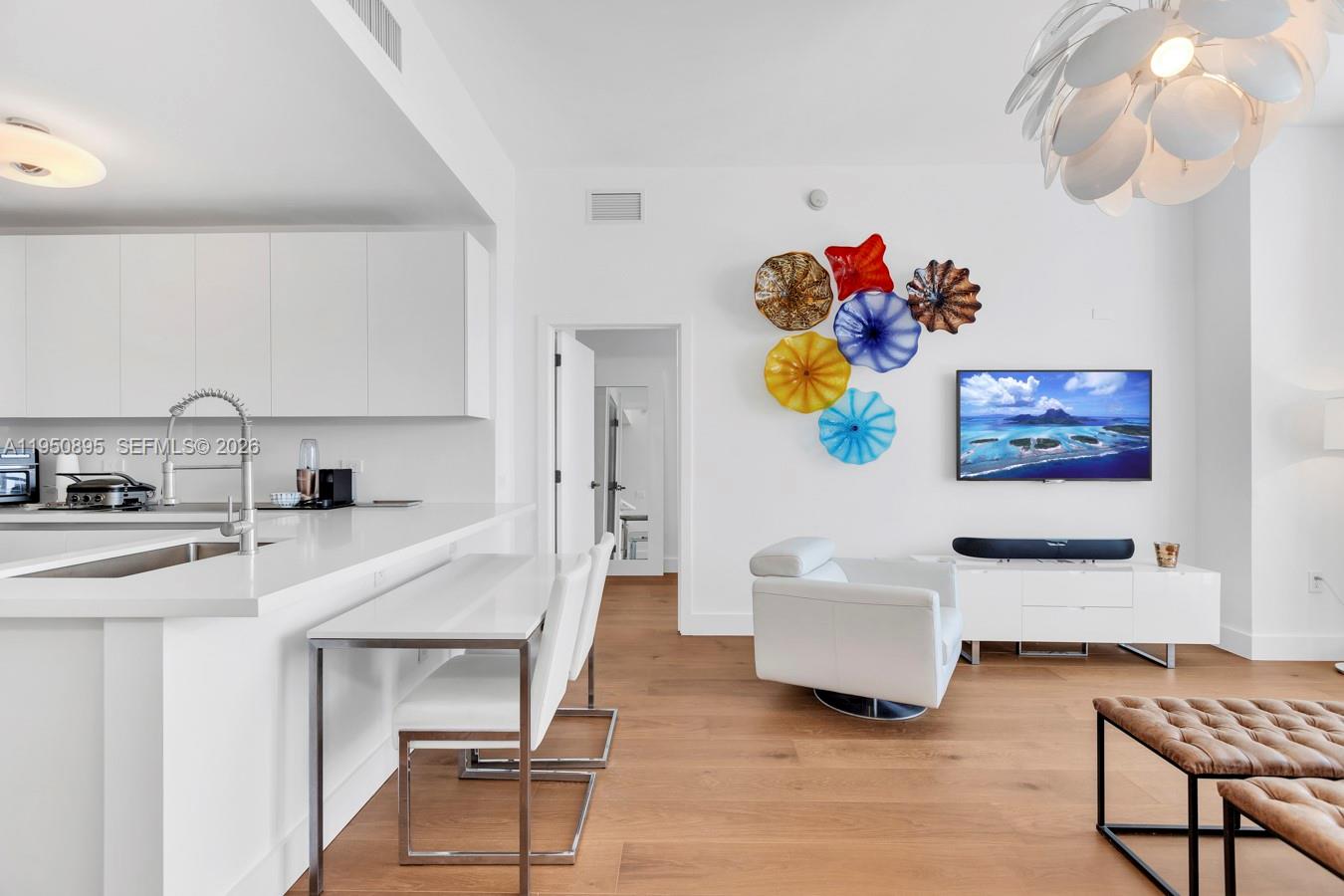 A modern living room and kitchen area feature white cabinetry, light wood floors, and wall art — 6799 Collins Ave # 412, Miami Beach FL 33141, MIAMI BEACH, FL