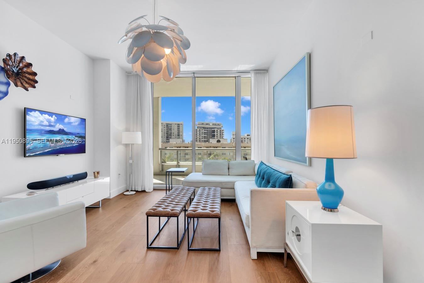 A bright living room features a white sectional sofa, two leather benches, and a balcony view — 6799 Collins Ave # 412, Miami Beach FL 33141, MIAMI BEACH, FL