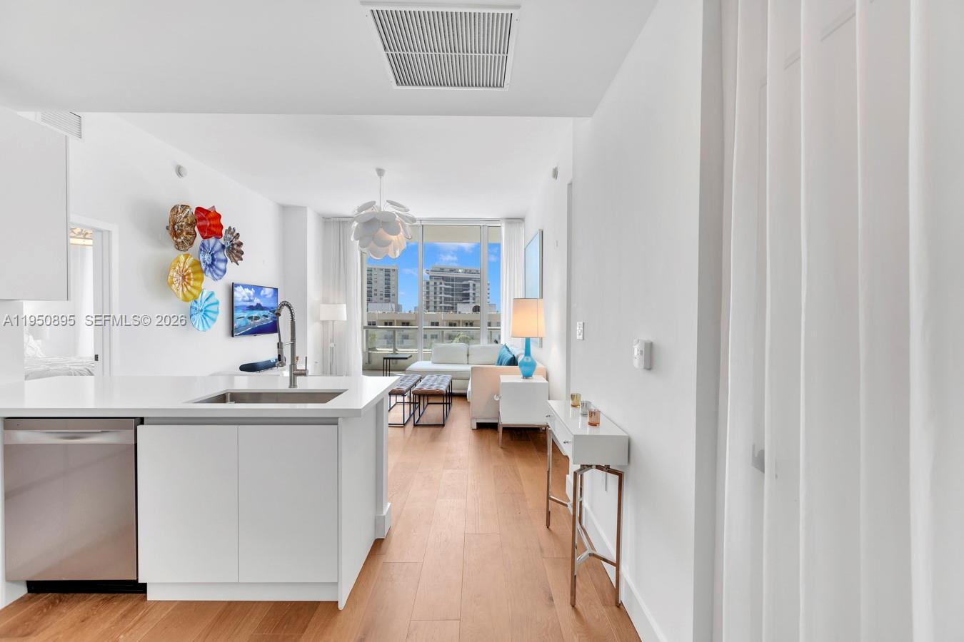 A modern kitchen island overlooks a living area with light wood floors and balcony views — 6799 Collins Ave # 412, Miami Beach FL 33141, MIAMI BEACH, FL
