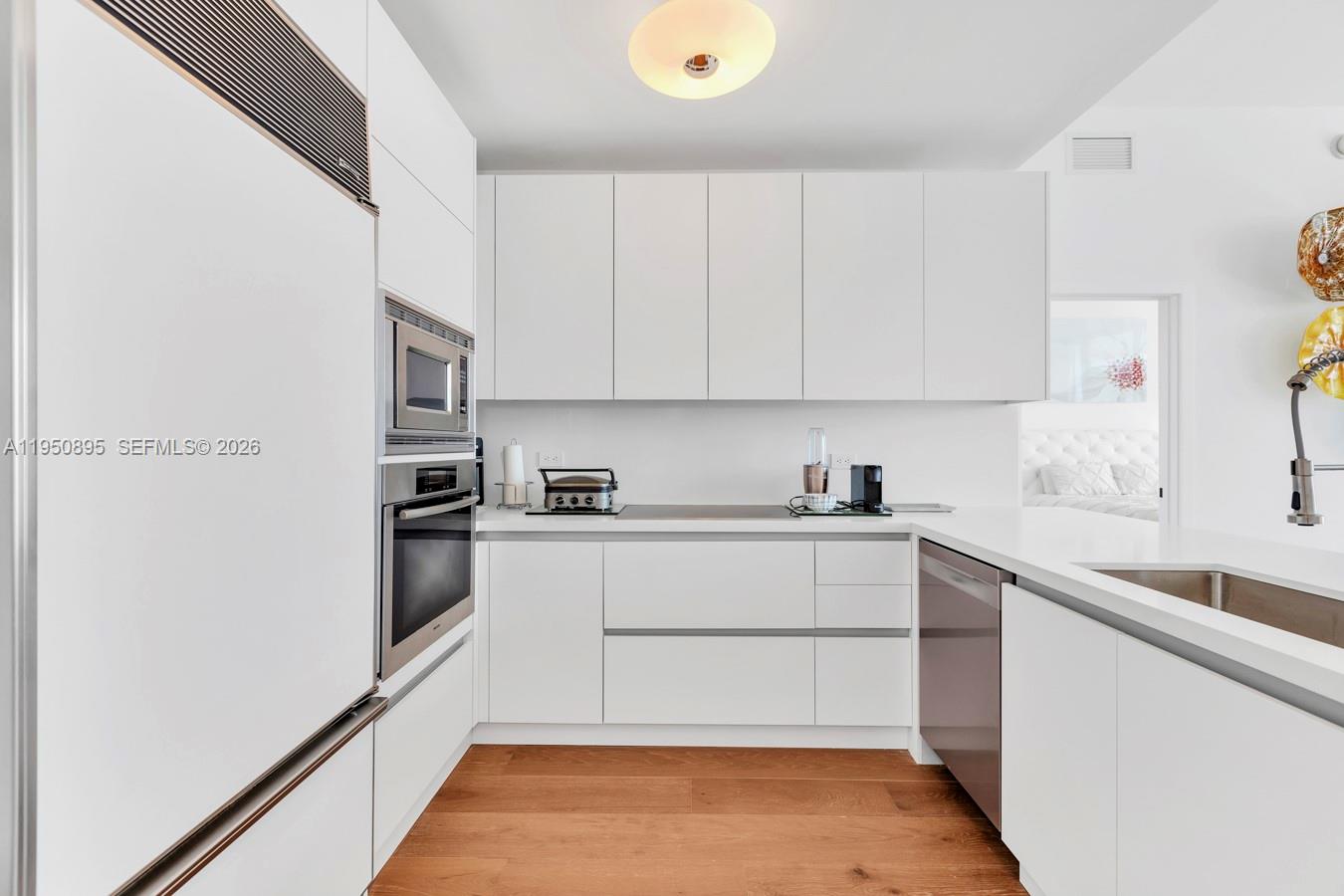 A modern kitchen features white cabinetry, stainless steel appliances, and light wood flooring — 6799 Collins Ave # 412, Miami Beach FL 33141, MIAMI BEACH, FL