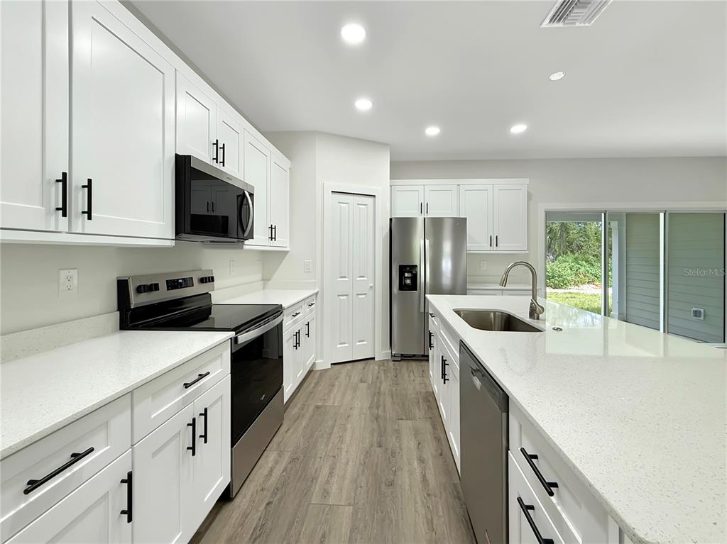 A modern kitchen features white cabinets, quartz countertops, stainless steel appliances, and wood-look flooring — 32 PURCELL STREET, PORT CHARLOTTE, FL