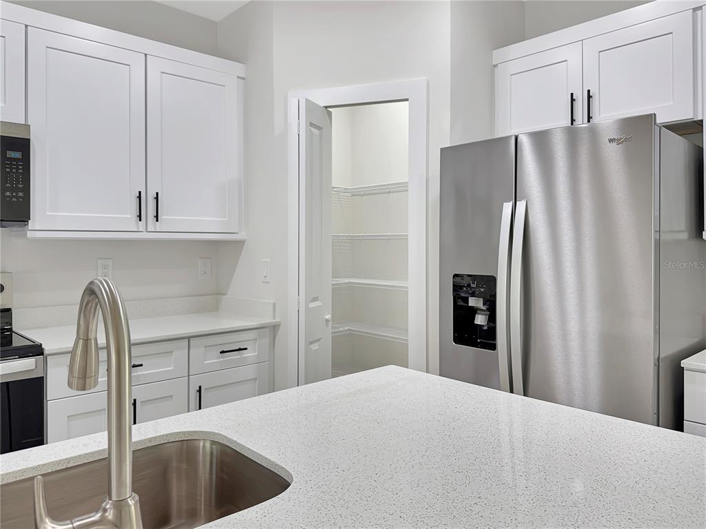 A kitchen features white cabinets, stainless steel appliances, a quartz island, and a walk-in pantry — 32 PURCELL STREET, PORT CHARLOTTE, FL